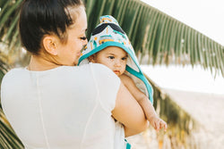 mum holding baby in blanket on beach